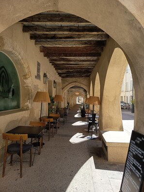 Un couloir intérieur avec des tables et des chaises en bois, un sol carrelé et un plafond haut avec des poutres apparentes.