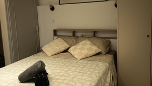 Een net opgemaakt bed met beddengoed met een patroon, een hoofdbord en een wandlamp.