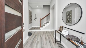 A hallway with a wooden door, a staircase, a mirror, and a sign on the wall.