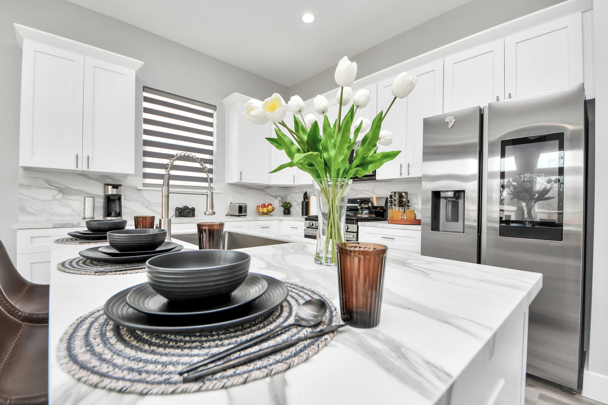 A modern kitchen with white cabinets, a stainless steel refrigerator, and a central island with a vase of white flowers.