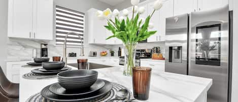Una cocina moderna con armarios blancos, un refrigerador de acero inoxidable y una isla central con un florero de flores blancas.