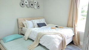 A bedroom with a bed, a bedside table, a window with curtains, and wall art.
