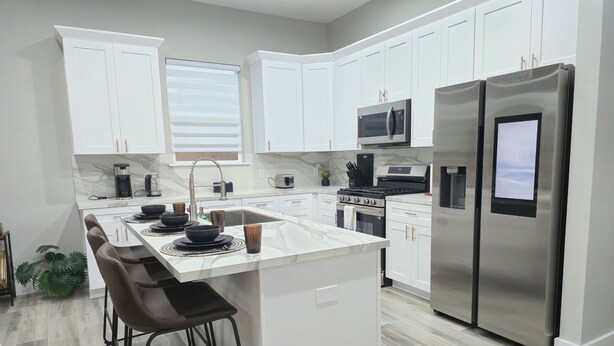 A modern kitchen with white cabinetry, stainless steel appliances, and a central island with bar stools.