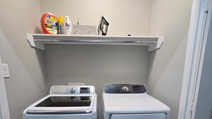 A laundry room with two front-loading washing machines and a shelf above containing cleaning supplies.