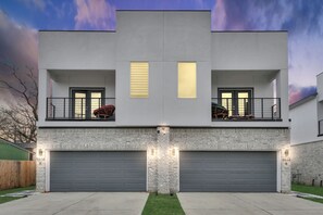 A modern two-story house with a garage, a balcony with a chair, and a well-maintained lawn. - Private Pool at Pershing Pad. 3BR Sleeps 10. 10 mins from NRG . Huge backyard (Houston)