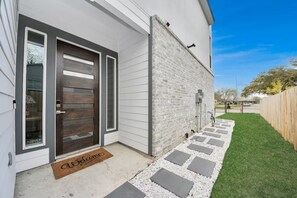 A modern house with a dark wooden door, white siding, and a brick wall. - Private Pool at Pershing Pad. 3BR Sleeps 10. 10 mins from NRG . Huge backyard (Houston)