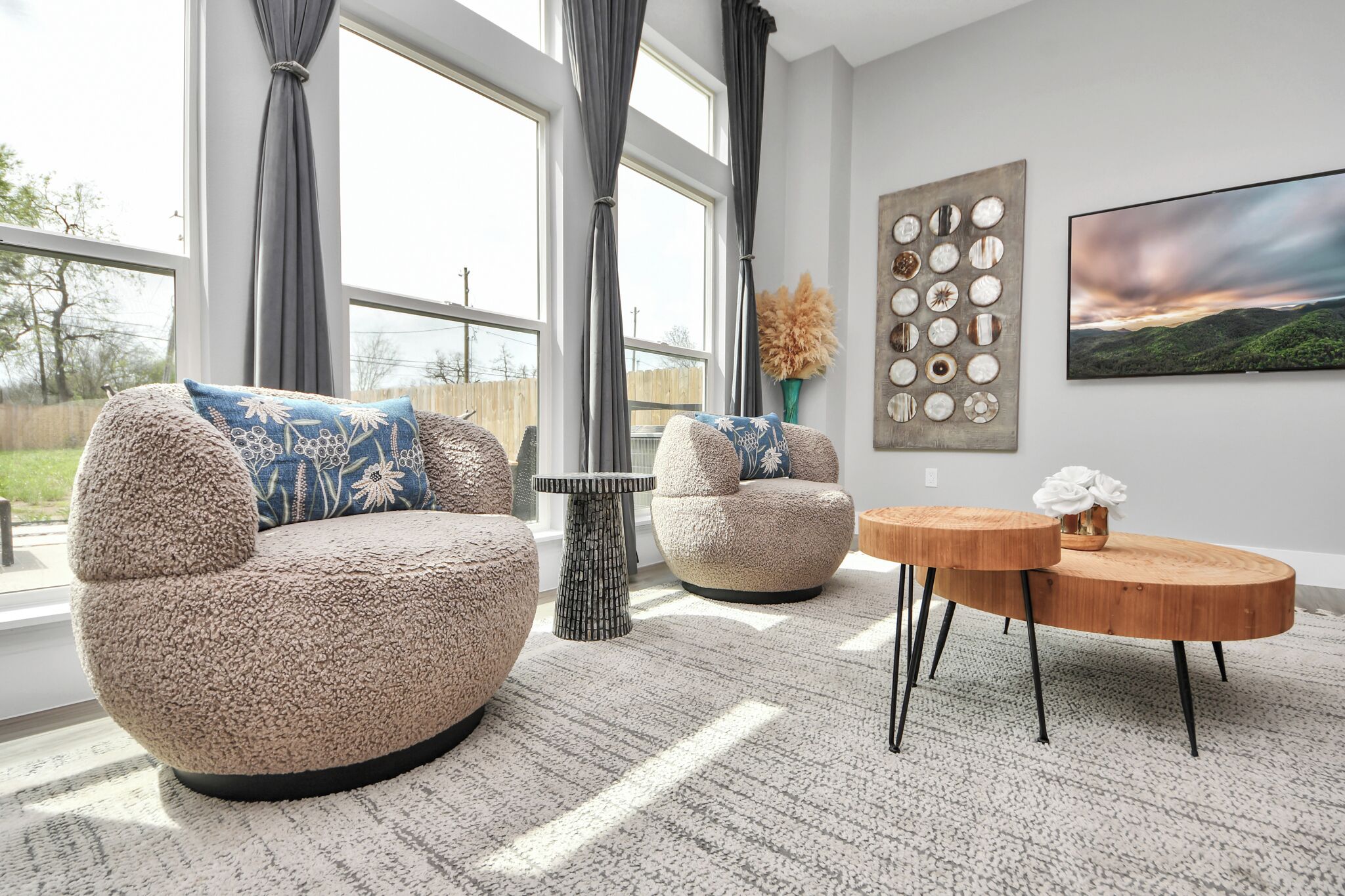 A modern living room with two round armchairs, a coffee table, and a large window with curtains.