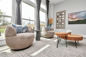 A modern living room with two round armchairs, a coffee table, and a large window with curtains. - Private Pool at Pershing Pad. 3BR Sleeps 10. 10 mins from NRG . Huge backyard (Houston)