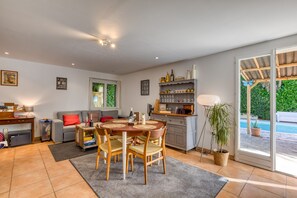 A spacious living area with a dining table, chairs, a sofa, a kitchen area, and a sliding glass door leading to a pool.