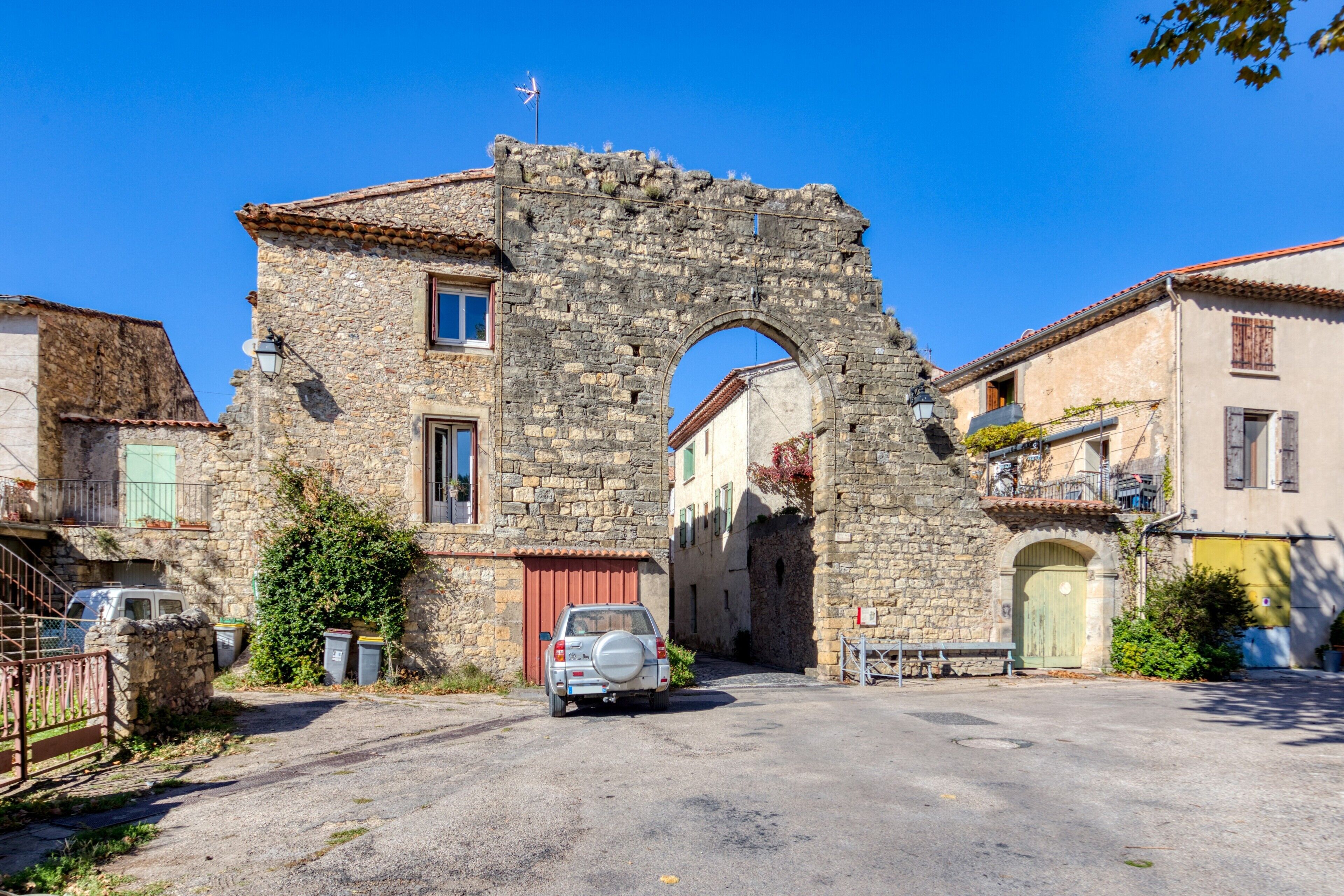A stone building with a large archway, a parked car, and a clear blue sky.