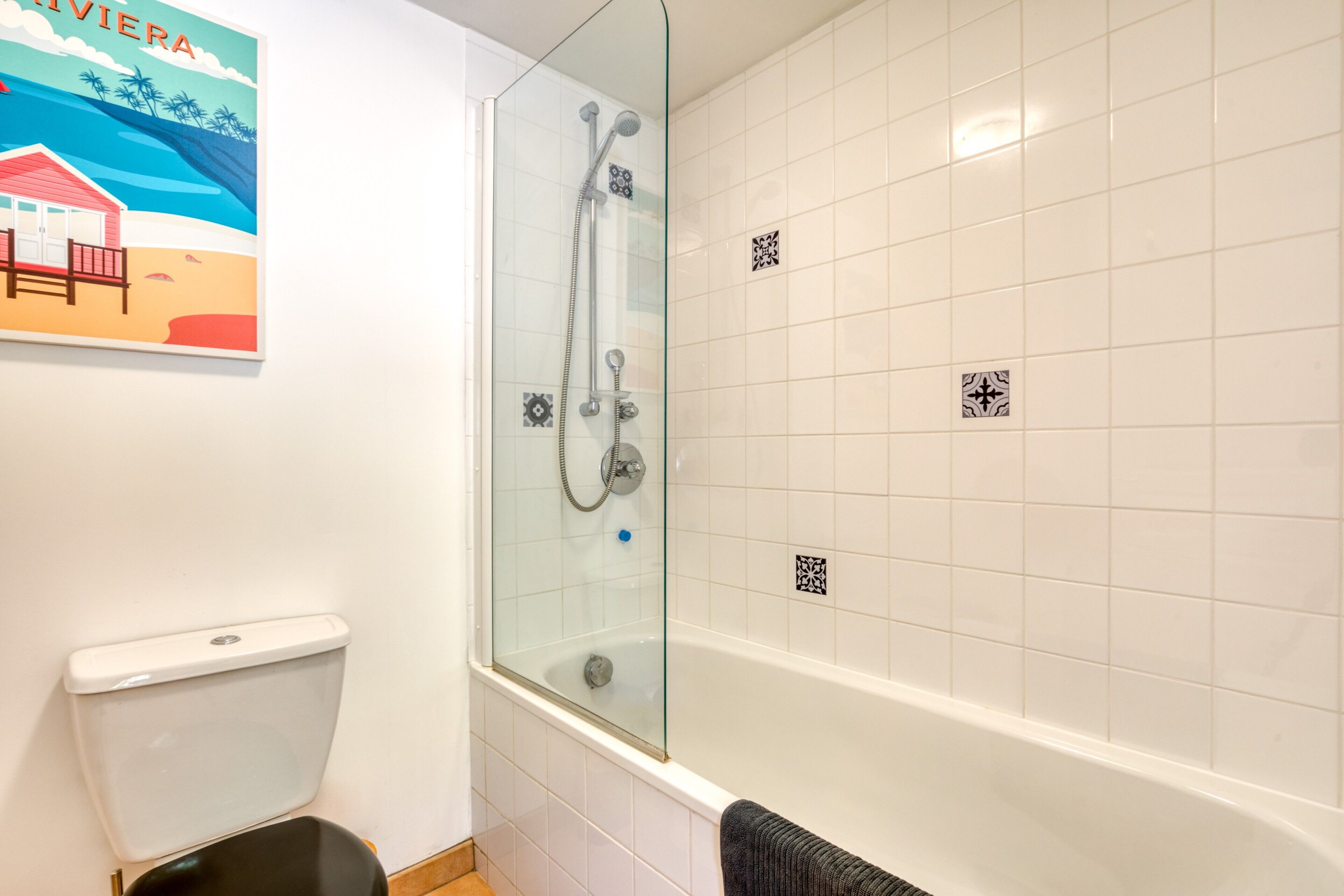A bathroom with a glass-enclosed shower, white tiled walls, a toilet, and a towel rack.