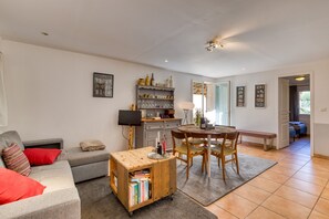 A living room with a sofa, a coffee table, a bookshelf, and a dining area with chairs and a table.