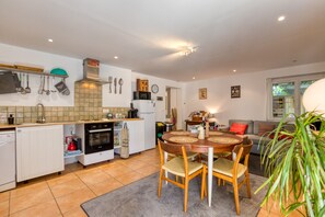 A compact kitchen with modern appliances, a dining area with a round table, and a living room with a sofa.