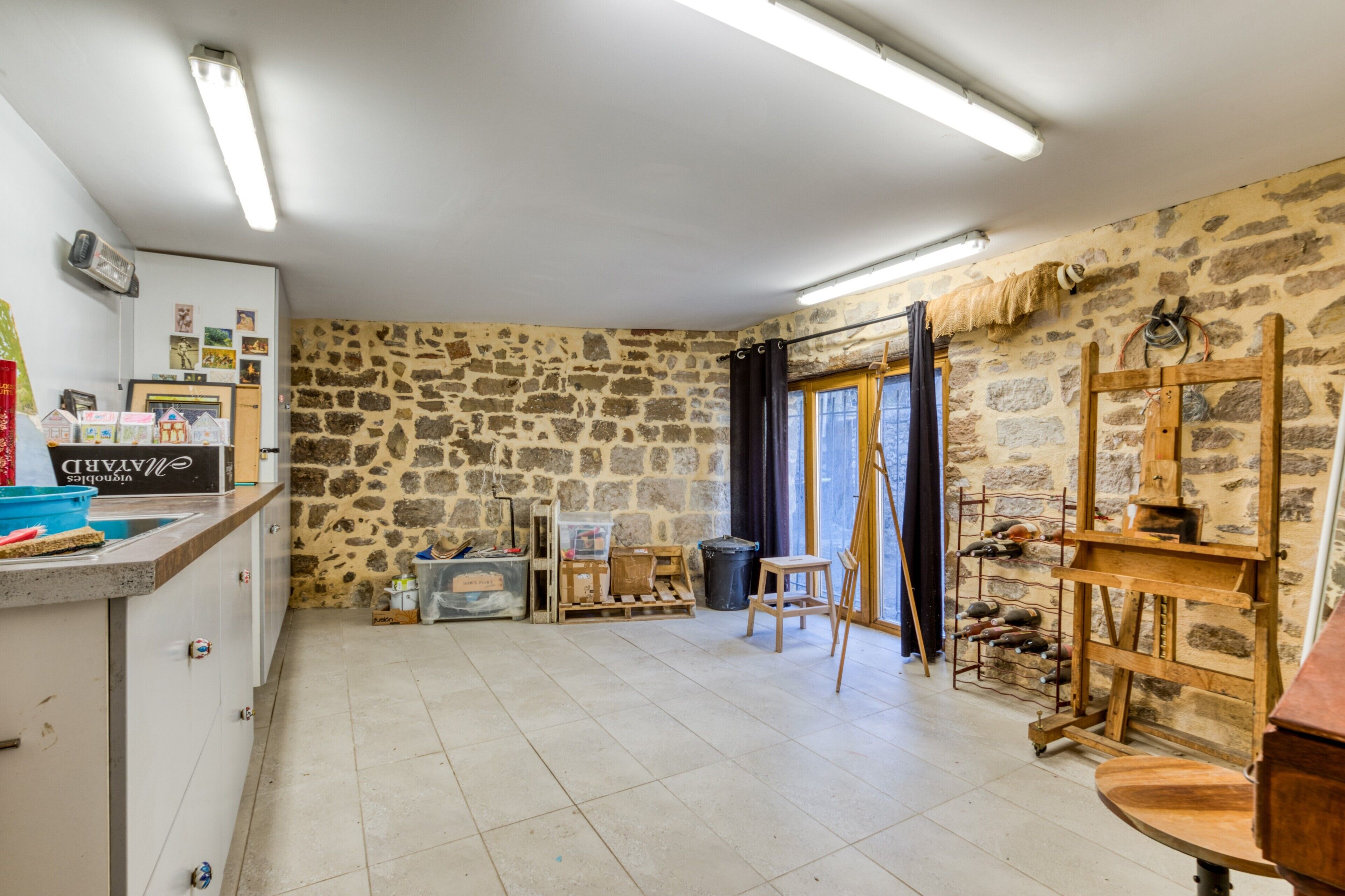 Una stanza con pareti in pietra, un cavalletto di legno, un lavandino e una finestra con vista.