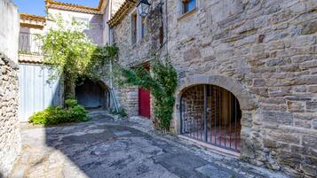 Une ruelle étroite pavée de pierres, avec une porte rouge et un portail en métal, bordée de bâtiments en pierre dotés de fenêtres en arc de cercle.