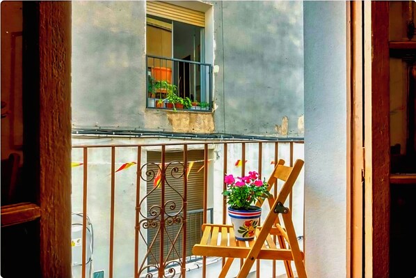 A balcony with a wooden chair, a potted plant, and a window with a view of a building.