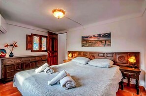 A neatly made bed with pillows and a rolled towel, a wooden nightstand with a lamp, and a painting on the wall.