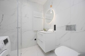 Ein modernes Badezimmer mit einer Duschkabine aus Glas, einem weißen Waschbecken mit Spiegel und einer Toilette.