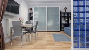 Een moderne woonkamer met een eethoek, een schuifpui naar een balkon en een blauwe opbergkast.
