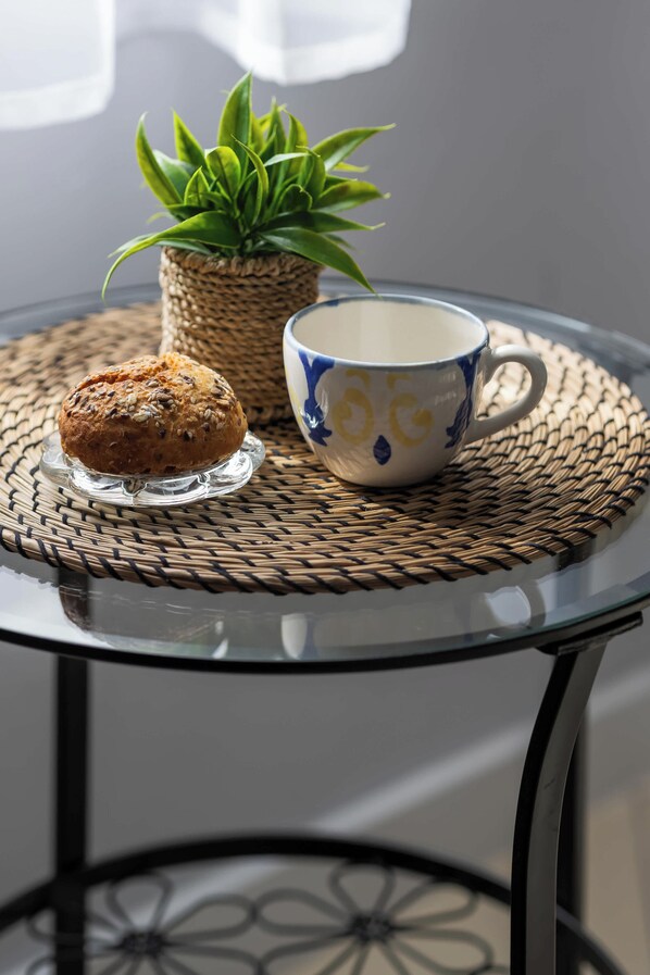 Una mesa con un mantel tejido, un plato de vidrio transparente, un muffin y una taza con un diseño azul y amarillo.