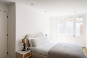 A bedroom with a bed, bedside table, lamp, and a window with a view.