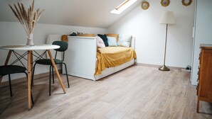Ein kleines Schlafzimmer mit Bett, Tisch mit Stühlen, Lampe und Heizkörper.