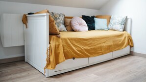 Ein Schlafzimmer im Loft-Stil mit einem weißen Bett, einer senfgelben Decke und verschiedenen Kissen.
