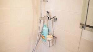 Ein Badezimmer mit weißen Fliesen, einer Dusche mit chromfarbenen Armaturen und einem an der Wand befestigten Seifenspender.