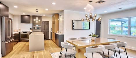 Una cocina moderna con una isla central, un comedor con una gran mesa y sillas, y un amplio ventanal con vistas al exterior.