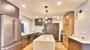 Una cocina moderna con electrodomésticos de acero inoxidable, una isla central, armarios de madera y un revestimiento de azulejos.
