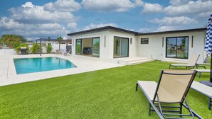 Una casa moderna con piscina, césped cuidado y un patio con mobiliario exterior.