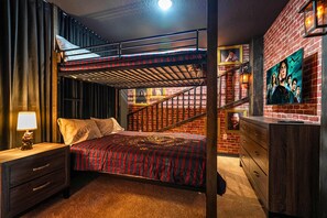Un lit superposé avec une couvre-lit à rayures rouges et noires, une table de chevet en bois avec une lampe et une commode avec un miroir.
