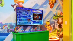Une console de jeux 3D dotée d’un écran affichant un menu de jeu, le tout entouré d’une décoration colorée sur le thème des dessins animés.