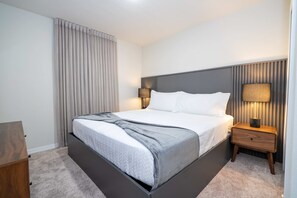 Une chambre d’hôtel moderne avec un grand lit, une table de chevet avec une lampe et une vue sur le paysage urbain par la fenêtre.
