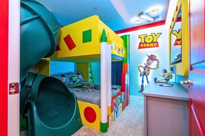 Une salle de jeux pour enfants avec un toboggan, un lit superposé et un mur décoré de personnages du film « Toy Story ».