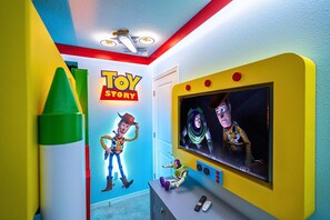 Une pièce avec un grand écran de télévision, une affiche des personnages de Toy Story et une figurine de Woody posée sur une étagère.