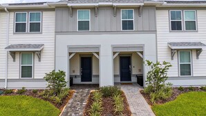 A two-story residential building with a symmetrical facade, a central entrance with double doors, and a small porch area. - Upstay Family Fun 5BR Retreat w Pool & Games Room (Clermont)