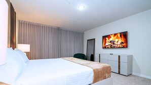 A hotel room with a bed, a television displaying a fireplace, a chair, and a wardrobe.