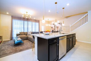 A modern kitchen with a central island, a dining area with a sofa, and a staircase leading to an upper level. - Upstay Family Fun 5BR Retreat w Pool & Games Room (Clermont)