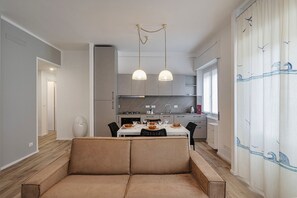 A modern kitchen with a dining area, featuring a sofa, pendant lights, and a view of the outside.
