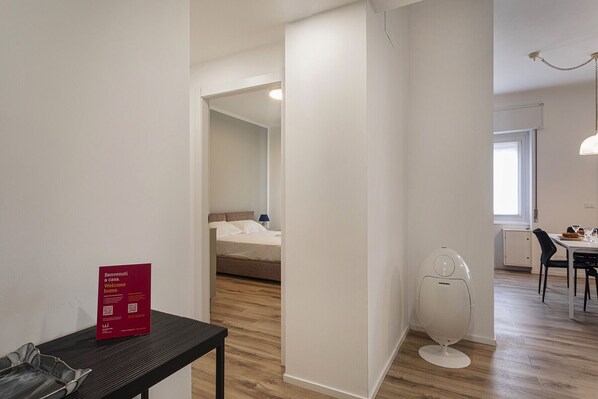 A hotel room with a bed, a small table with a red sign, a toilet, and a view of a dining area.