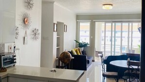 A modern living room with a large window, a dining area with a round table, and decorative wall art. - 1 Bedroom Mountain Retreat New Kingston (Kingston)