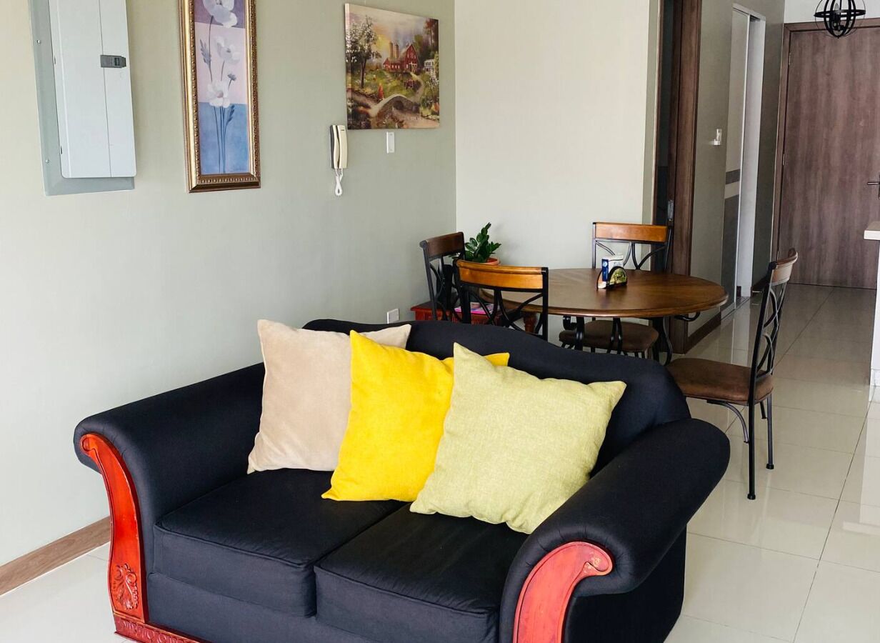 A living room with a dark blue sofa, a wooden dining table, and a painting on the wall.