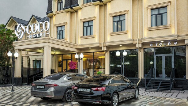 A hotel with a prominent 'Coco Hotel' sign, a 'Tour' entrance, and two cars parked in front. - COCO HOTEL (Tashkent)