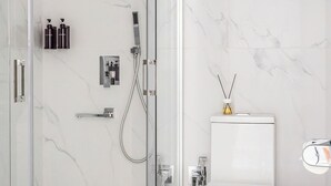 A modern bathroom with a glass-enclosed shower, a toilet, and a trash can.