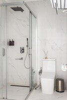 Moderni kylpyhuone, jossa on lasiseinällä varustettu suihku, wc ja roskakori.