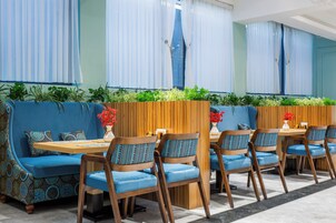 A restaurant with blue upholstered seating, wooden tables, and green plants.