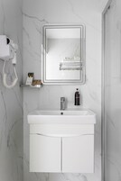 A bathroom with a white sink, a mirror, a hairdryer, and a shelf with toiletries.