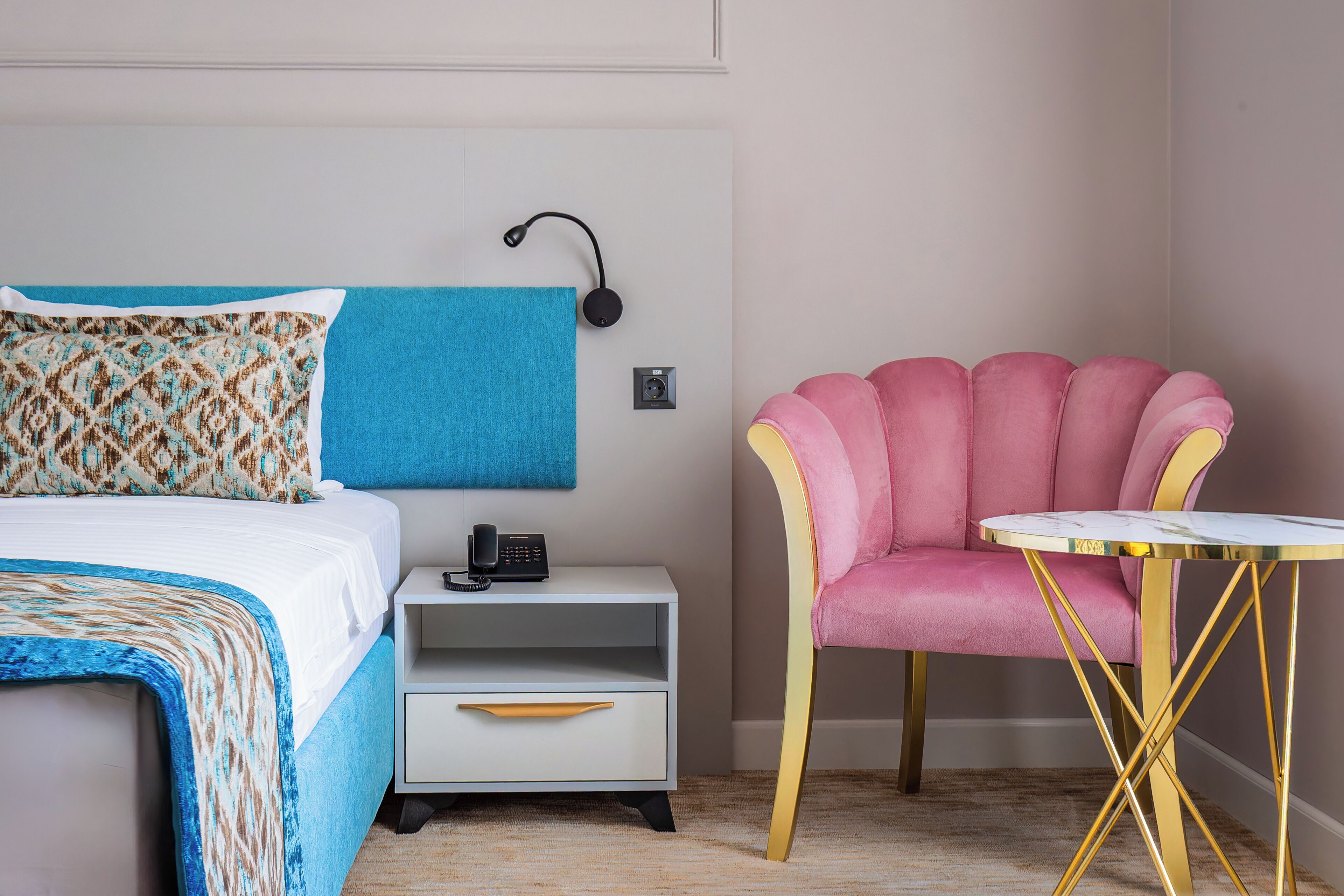 A hotel room with a bed, a bedside table with a telephone, a chair, and a small round table.