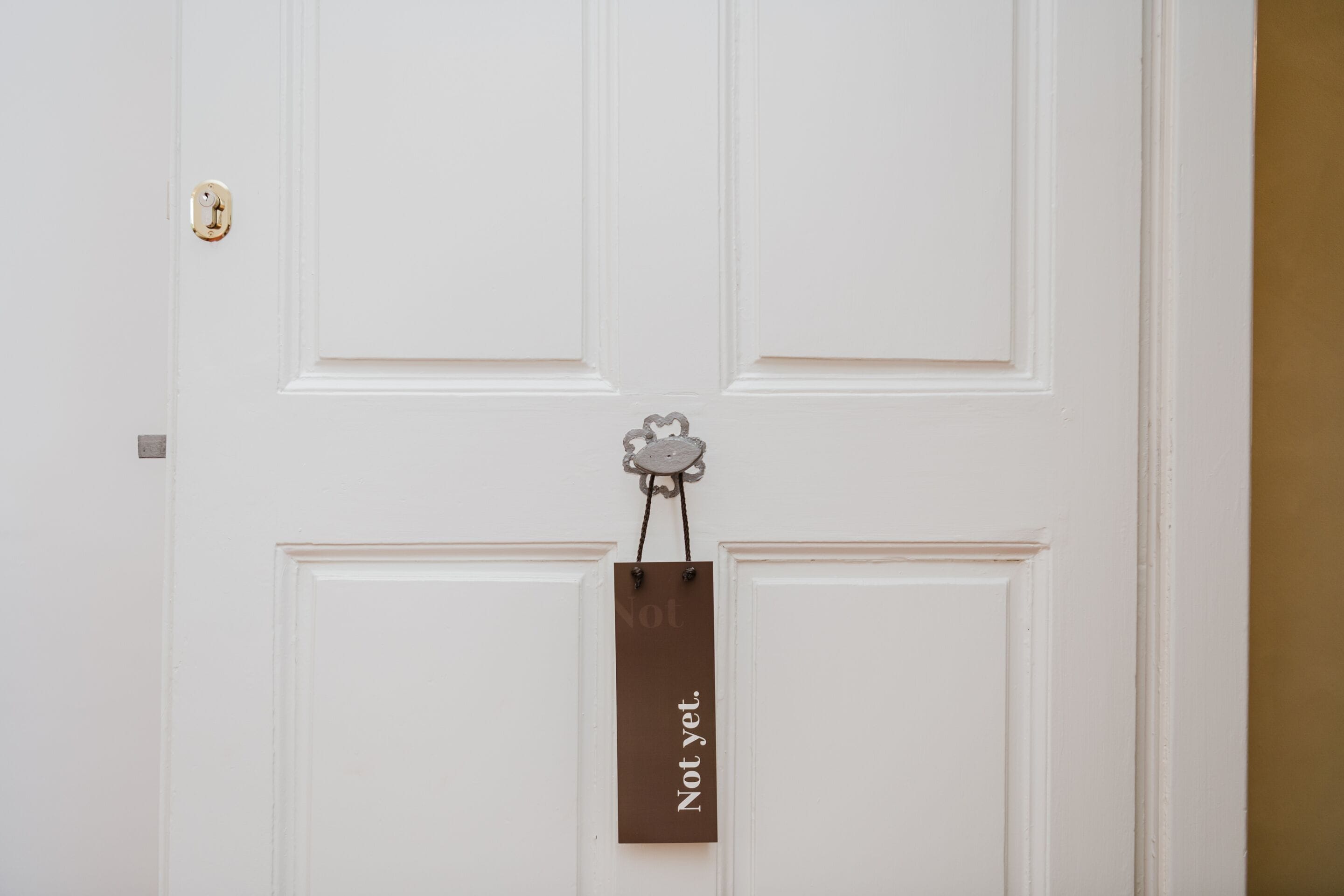 A white door with a keyhole and a small metal object hanging on the door.